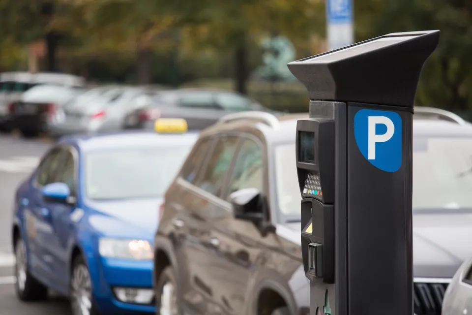 Parking payment machine on street with blurred cars parked in background.